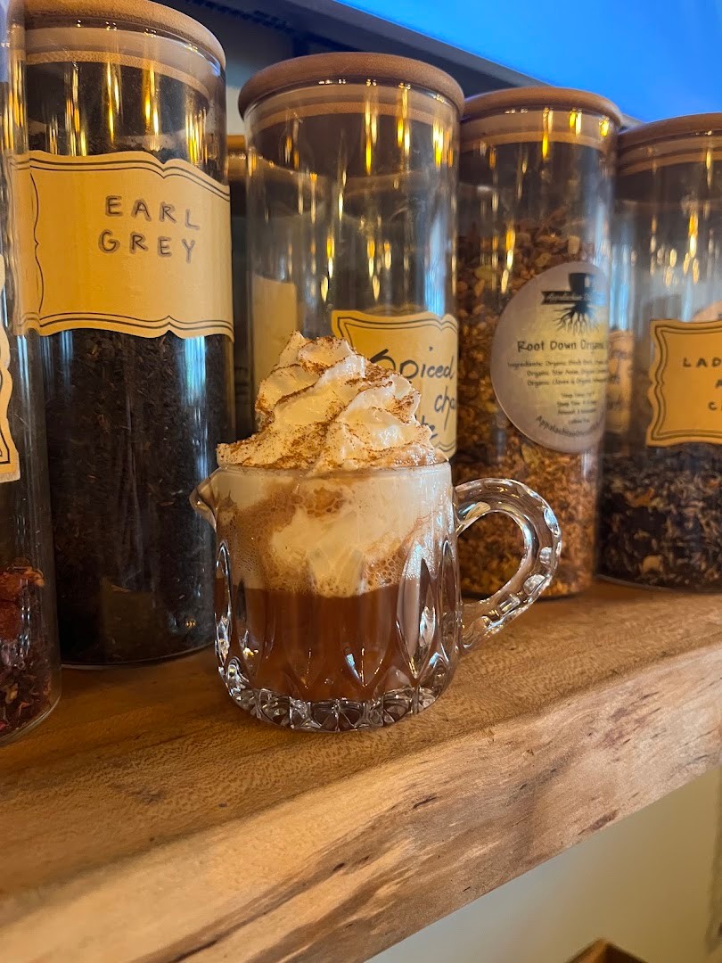 A hot cacao with whipped cream in front of jars of loose-leaf tea